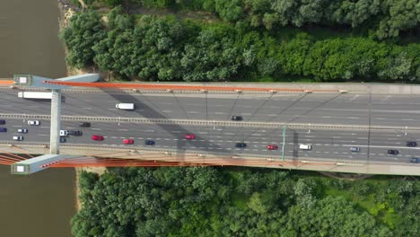 Stadtauto-Bewegt-Sich-An-Der-Autobahnbrücke-Auf-Hintergrund,-Glatter-Flussoberfläche,-Drohnenansicht