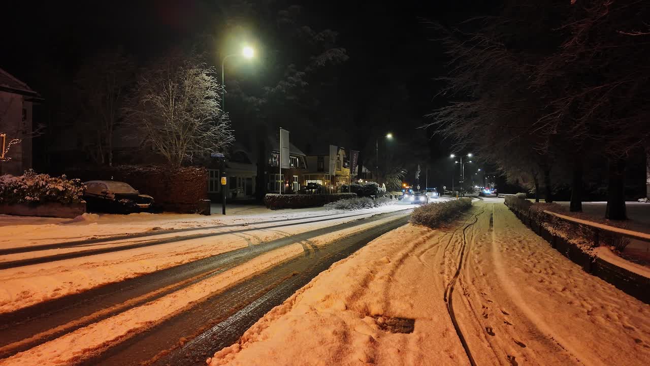 Auto che guida su una strada innevata e ghiacciata in una fredda notte invernale. Gli spazzaneve guidano sullo sfondo e mantengono pulite le strade.