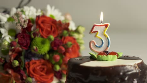arreglo de flores mixtas y pastel de cumpleaños con vela encendida número 3