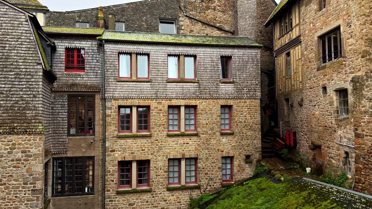 Edifici in pietra con accenti rossi alle finestre nella zona storica di Mont-Saint-Michel. Adatto per studi architettonici o articoli di viaggio.