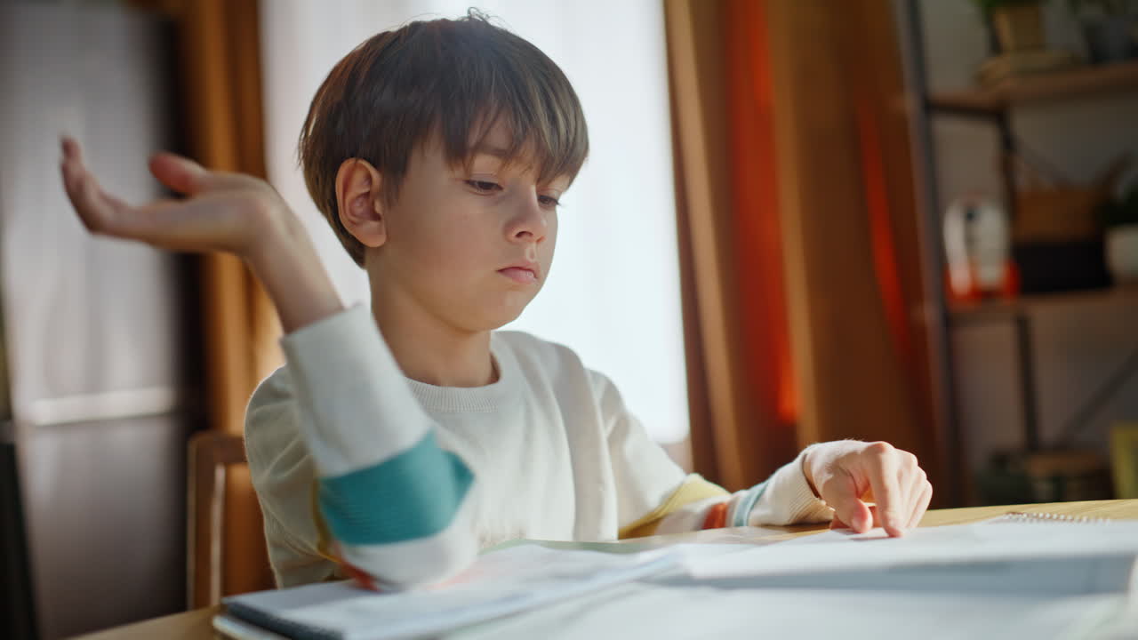 Ragazzo serio che si prepara per gli esami, scrive sul quaderno seduto al tavolo della cucina di casa, primo piano.
