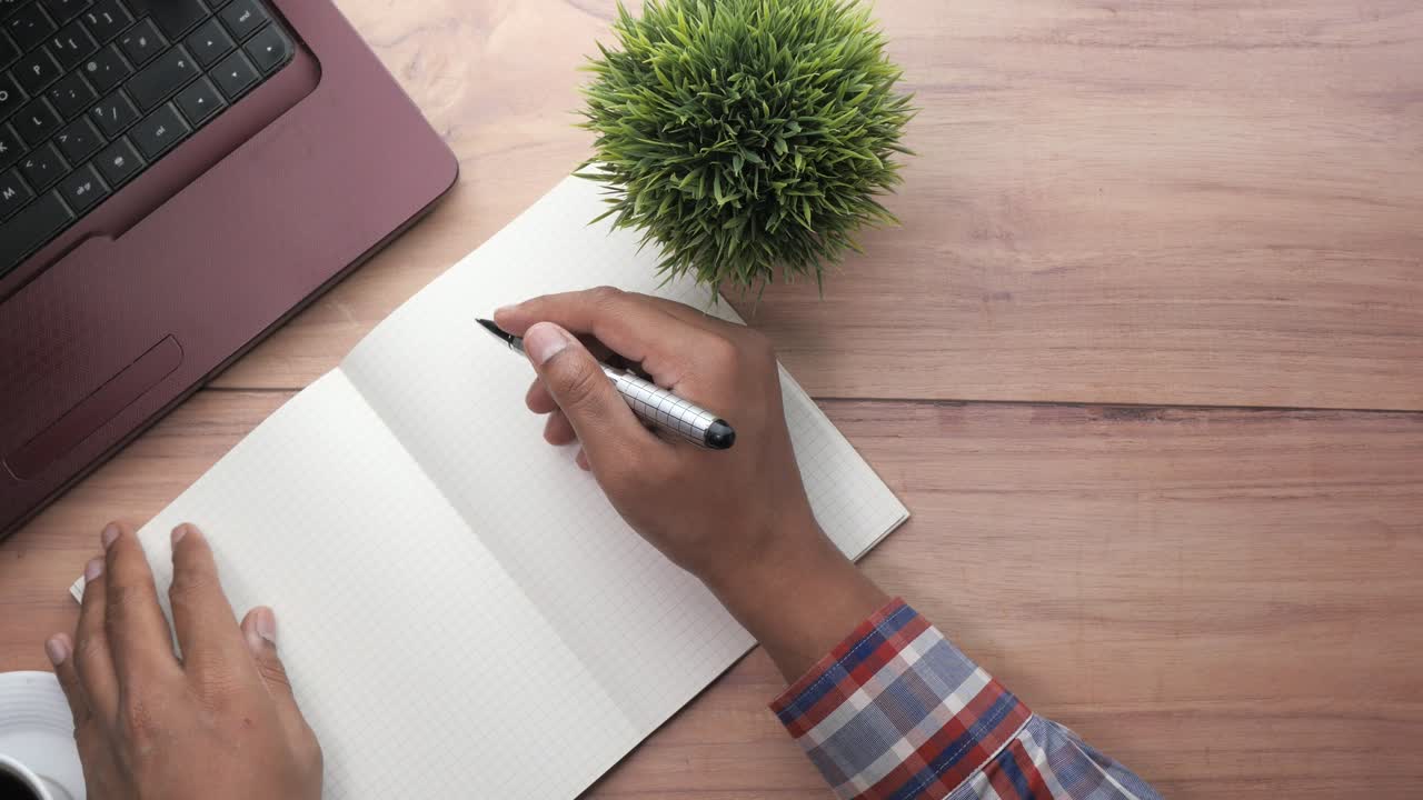 Person writing in notebook at a desk with a laptop