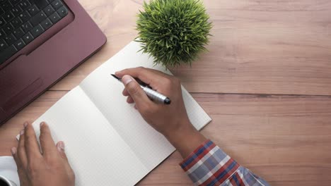 person writing in notebook at a desk with a laptop