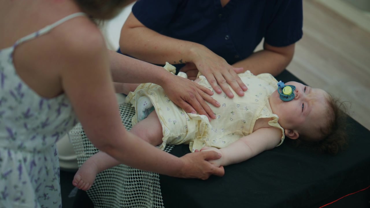 Bambino sdraiato su un tappetino mentre due adulti confortano e sostengono delicatamente il bambino durante un tranquillo momento di cura al chiuso