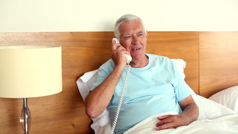 senior man sitting in bed answering the phone