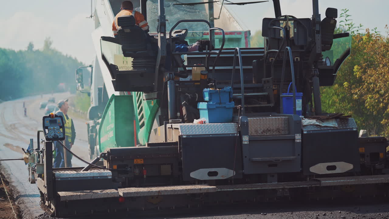 Asphalt paver and workers on the road. Fresh asphalt resurfacing the street. Workers in a huge machinery for making a new road. Roadworks outdoors.