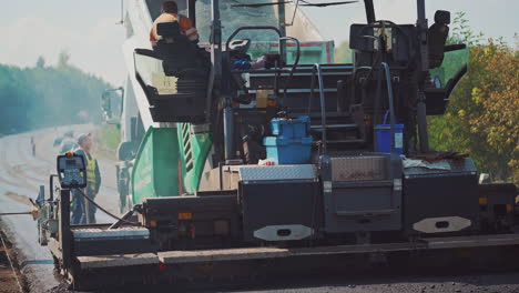 asphalt paver and workers on the road. fresh asphalt resurfacing the street. workers in a huge machinery for making a new road. roadworks outdoors.