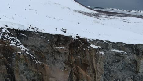 Vista-De-Drones-En-La-Zona-De-Tromso-En-Invierno-Volando-Sobre-Una-Montaña-Nevada-Y-Mirando-Hacia-El-Acantilado-Hacia-El-Fiordo-En-Segla,-Noruega