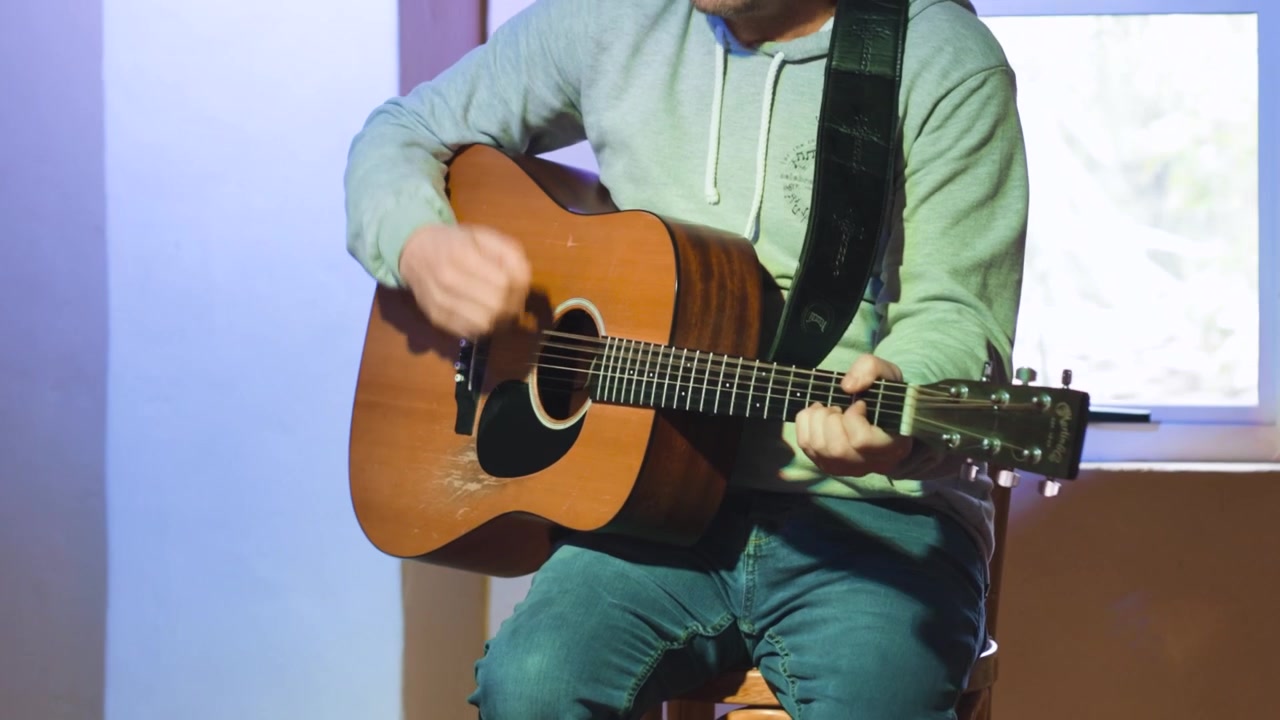 Gitarr spelas energiskt av man. Halvnära bild som följer åt vänster.