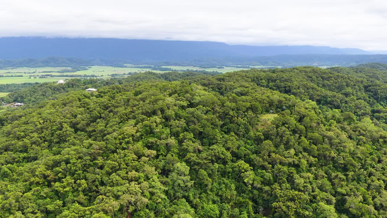 Drone glides above green forest and farmland, revealing valley landscape under soft daylight