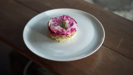 traditional russian salad with beetroot and herring vegetables, lying on a wooden table in a white plate