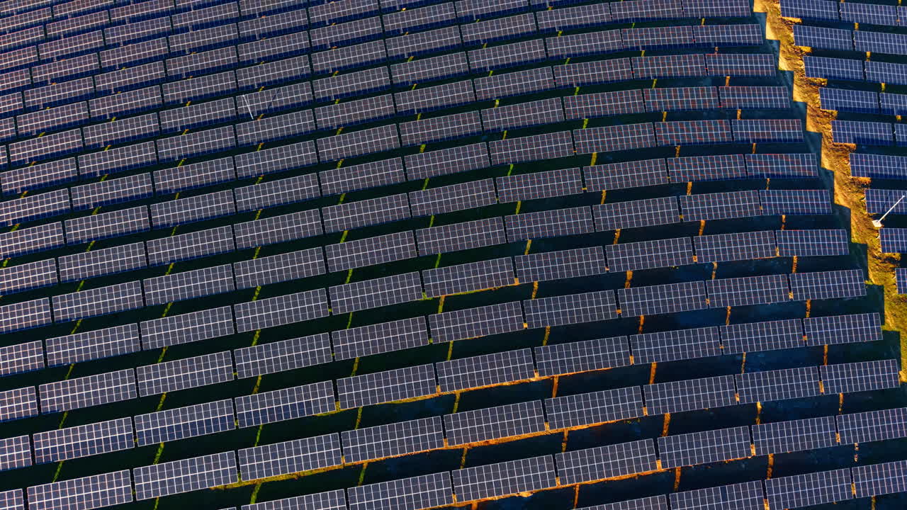 Fitte file di pannelli solari con riflesso della luce del tramonto. Prospettiva aerea di una grande schiera fotovoltaica con calda luce solare che illumina il terreno tra le file.