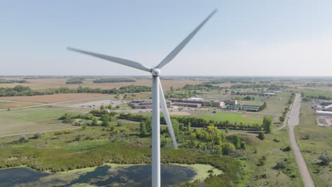 Vista-Aérea-De-Una-Turbina-Eólica-Giratoria-Con-Una-Escuela-Secundaria-Rural-Americana-En-El-Fondo,-Concepto-De-Energía-Renovable-Que-Impulsa-La-Educación