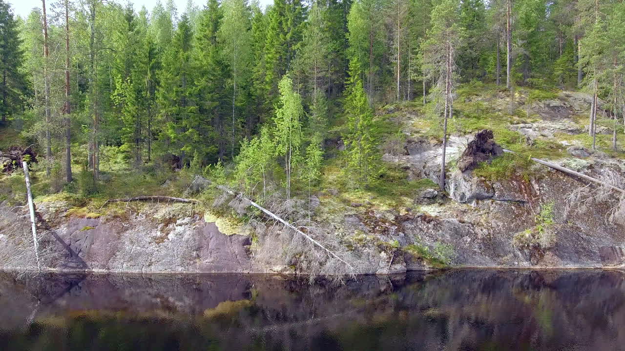 drone deslizándose frente a un acantilado empinado sobre un tranquilo lago forestal en el desierto boreal
