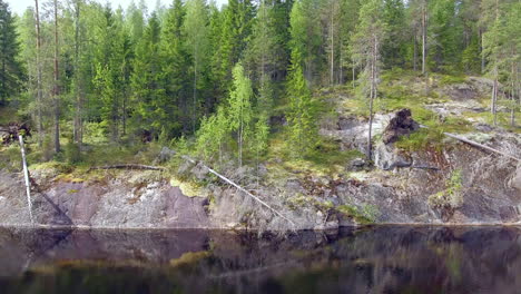 drone sliding in front of a steep cliff above a calm forest lake in the boreal wilderness