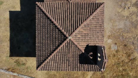 rising-flight-with-overhead-view-of-the-roof-of-a-hermitage-with-brown-tiles-with-its-bell-tower-in-a-meadow-with-a-stone-wall-in-summer-during-the-day-in-Avila-Spain