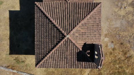vuelo ascendente con vista aérea del techo de una ermita con azulejos marrones con su campanario en un prado con una pared de piedra en verano durante el día en ávila-españa