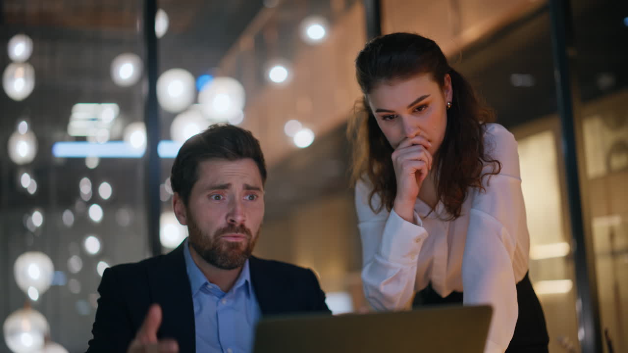 Desperate colleagues looking computer reacting on loss at night office closeup