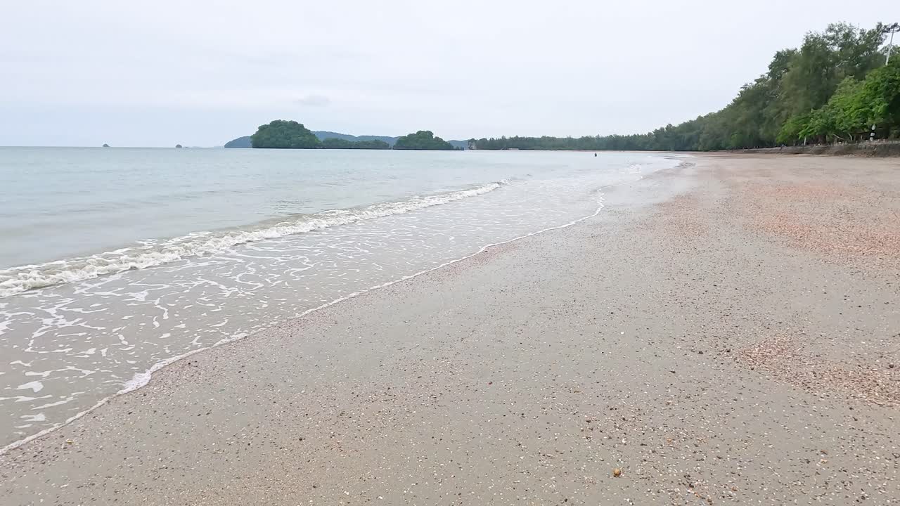 태국 크라비의 조용한 해변 장면, 부드러운 파도와 부드러운 자연 조명 아래 울창한 초록색을 보여줍니다.