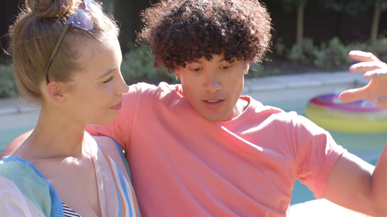 Young diverse couple relaxing by pool, enjoying sunny day and sharing laughter together