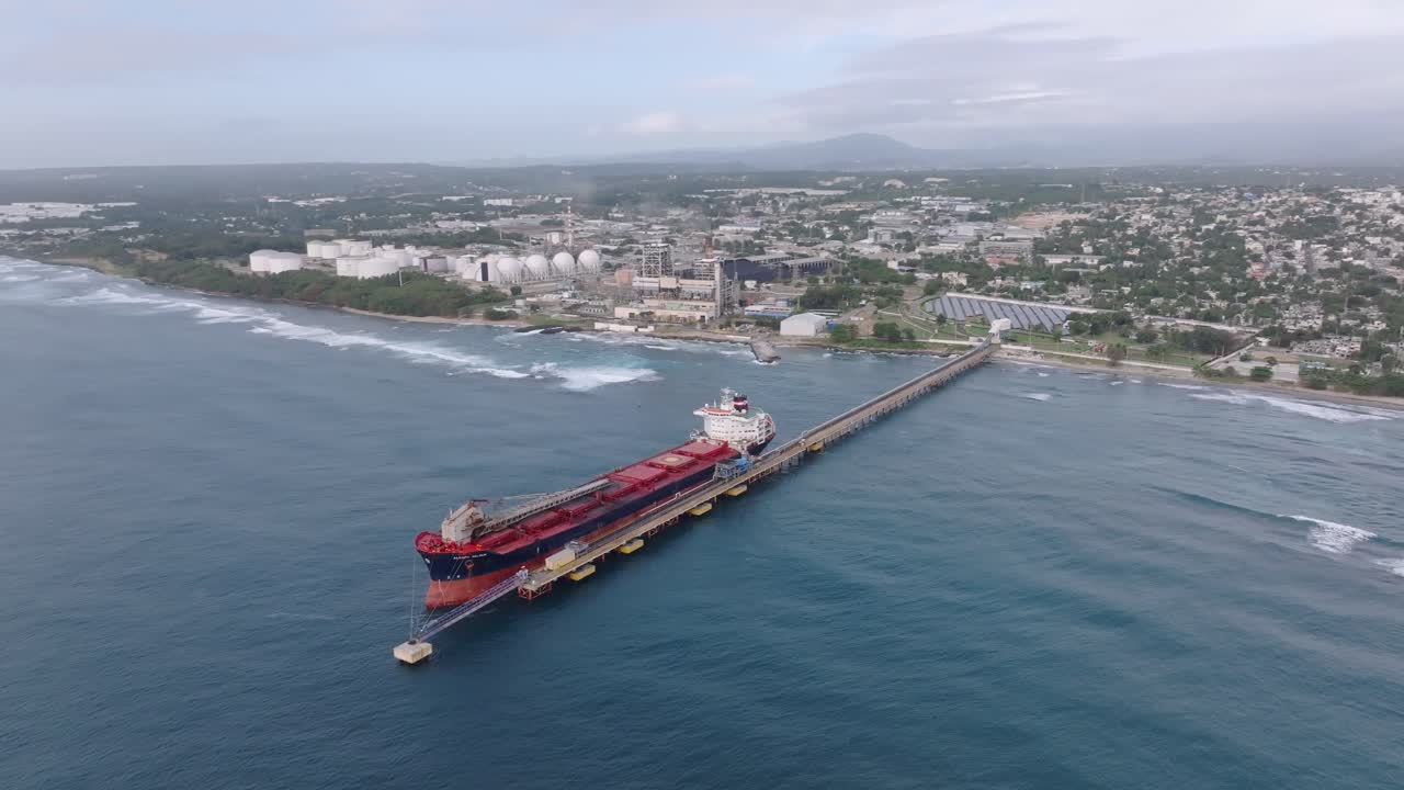 Oil tanker docked at Port of Haina with industrial infrastructure and urban landscape, energy distribution, maritime transport, and trade, Dominican Republic. Aerial orbiting