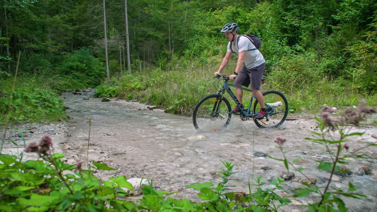 Man cycles through a small river on a mountain bike. Slowmotion shot. Adventure activity. Topla Valley, Slovenia