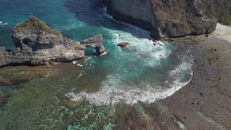 Aerial-view-of-Atuh-beach-on-Nusa-Penida,-Indonesia-on-a-sunny-day-and-with-crystal-blue-water-hitting-the-rock-formations