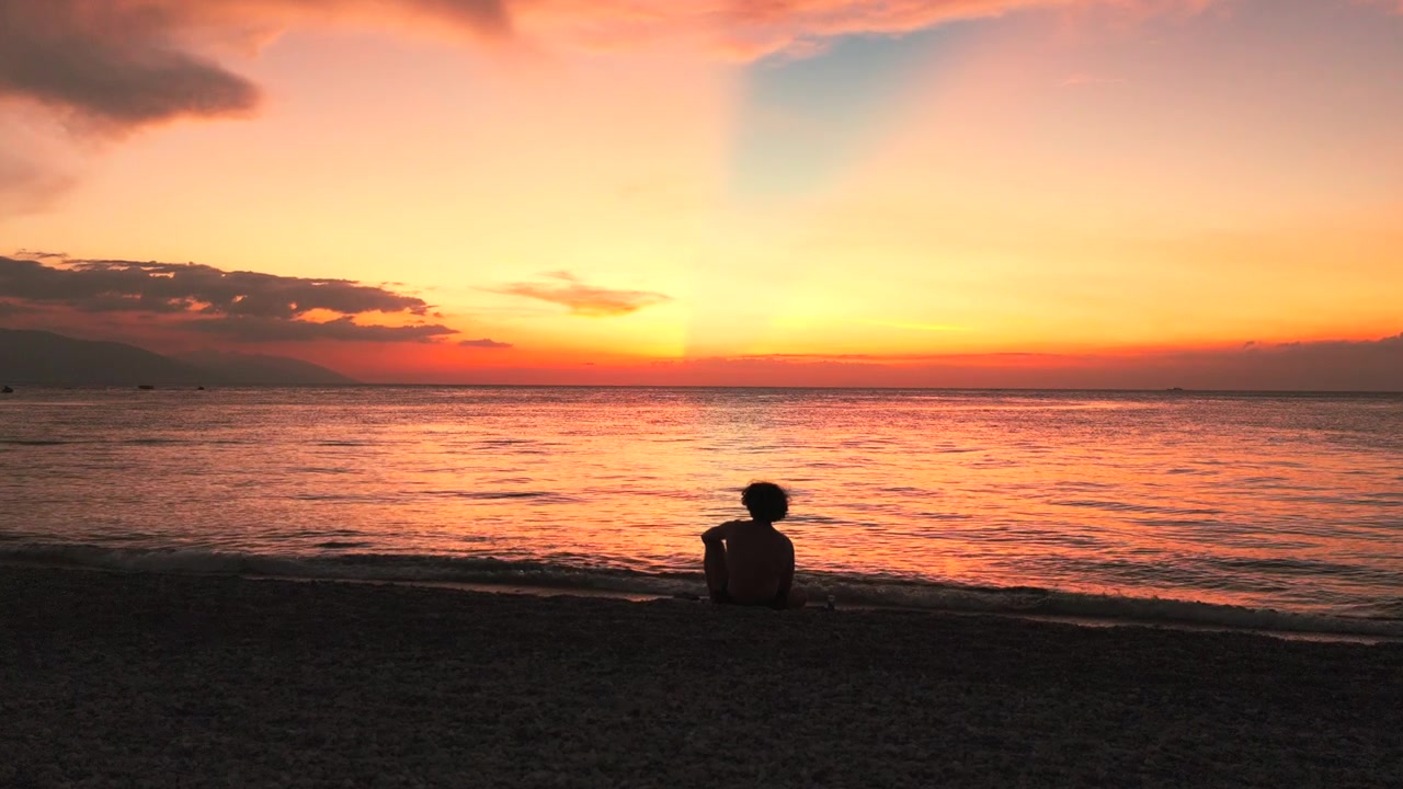 Persona seduta da sola su una spiaggia tropicale durante un tramonto colorato nelle Filippine