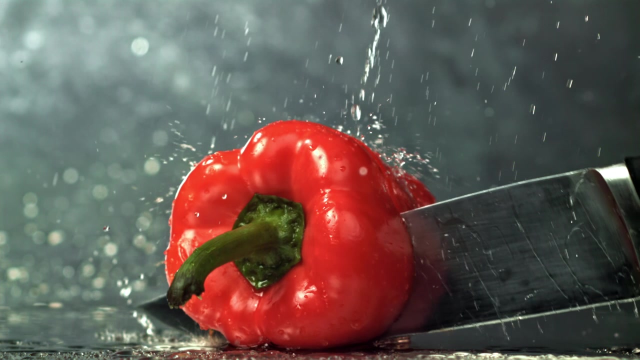 Čerstvá červená paprika nakrájená nožem s cákající vodou.