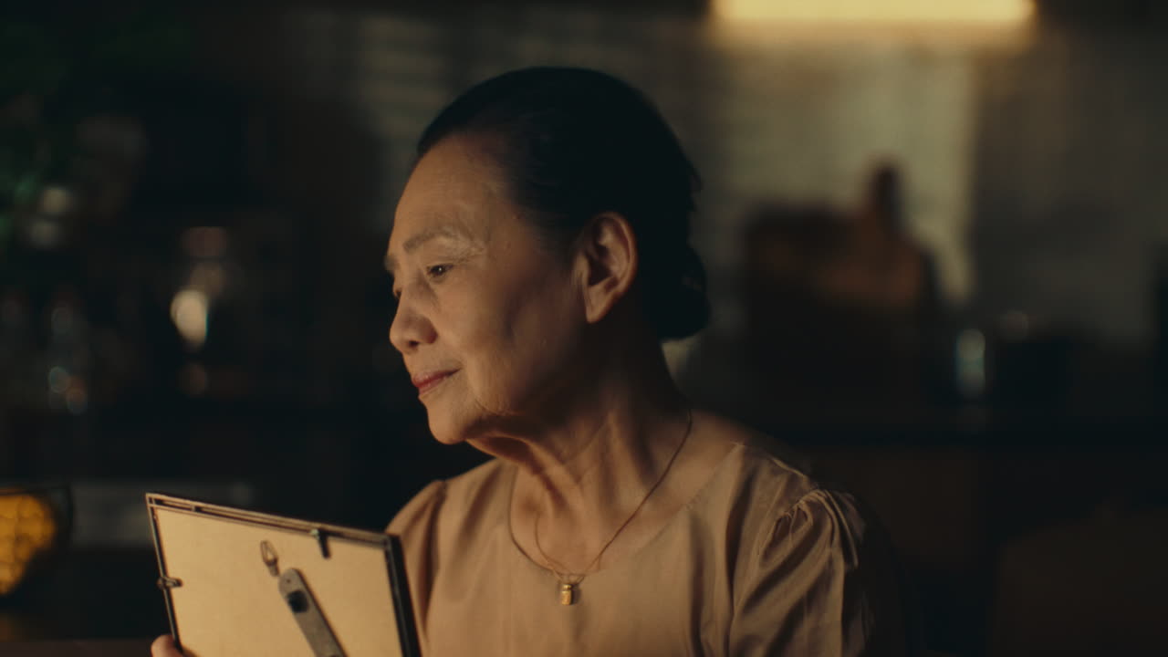 Elderly woman reminiscing while looking at an old photo in a warm, nostalgic moment