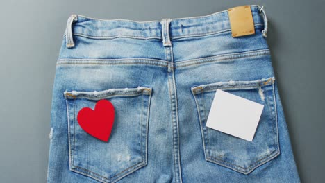 close up of jeans with heart and white note on grey background with copy space