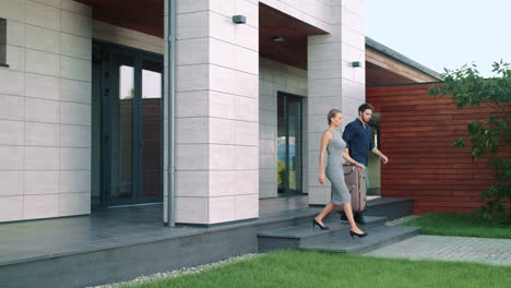 una pareja rica sale de casa con equipaje. una pareja hermosa sale de una casa grande.