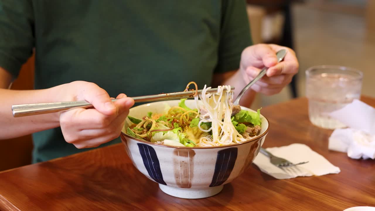 Primo piano di una persona che usa le bacchette per mangiare bun cha vietnamita in un ristorante.