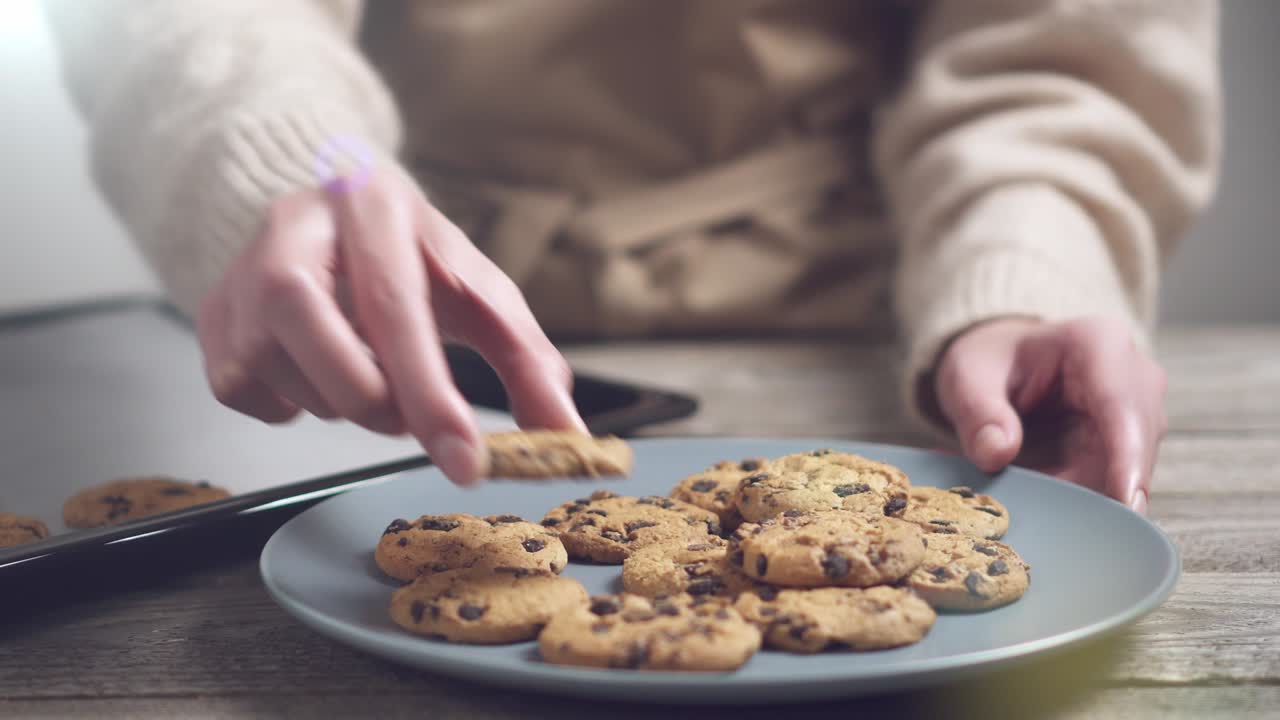 페르가멘트 종이로 인 베이킹 시트 위에 집에서 만든 초콜릿  쿠키. 베이지 스웨터를 입은 소녀가  접시 위에 쿠키를 놓는다.