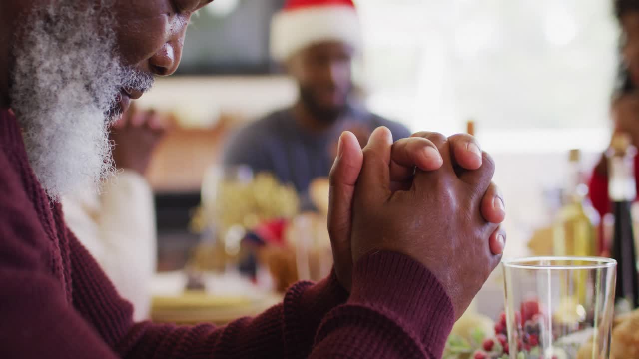 familia afroamericana con sombreros de santa, tomados de la mano y orando.