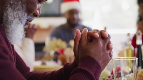 african american family wearing santa hats holding hands and praying