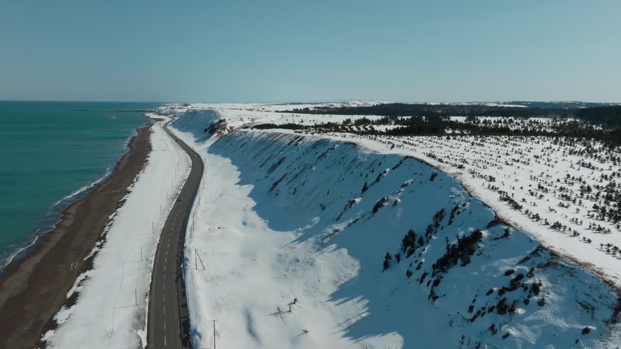 National Highway With Two Lanes Passing By The Sea And Snowy Hills In Winter In Japan. - aerial shot