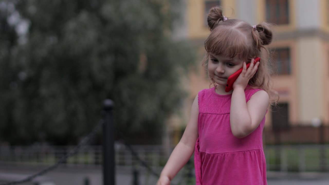 niña hablando por teléfono inteligente al aire libre. niño con vestido rosa hablando por teléfono móvil en la calle de la ciudad