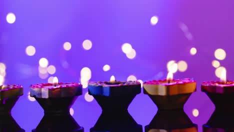 Close-up-of-burning-colourful-candles-celebrating-diwali-on-purple-background