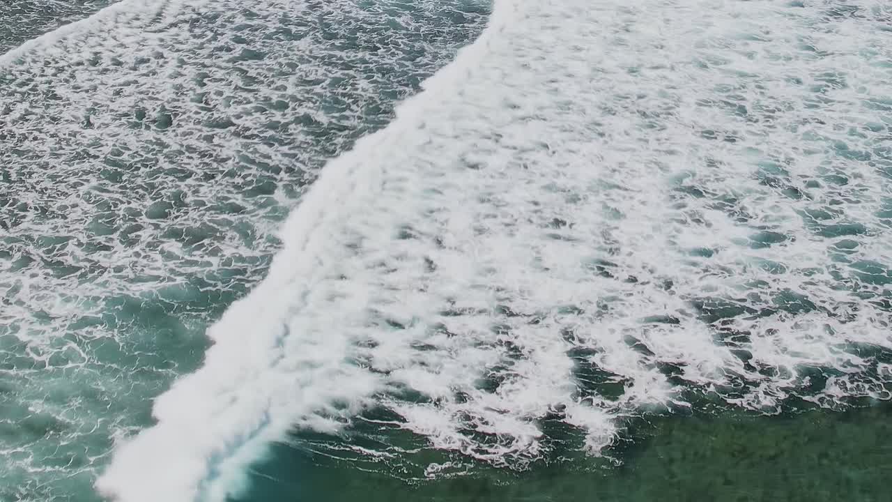 Waves crash on clear waters near a surfer in the Canary Islands in Spain