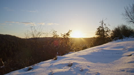 Low-angle-shot-of-walking-in-the-snow,-camera-moves-forward-towards-some-trees-into-the-sun