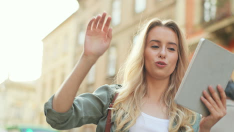 Close-up-view-of-blonde-young-woman-making-a-video-call-on-the-tablet-and-walking-down-the-street