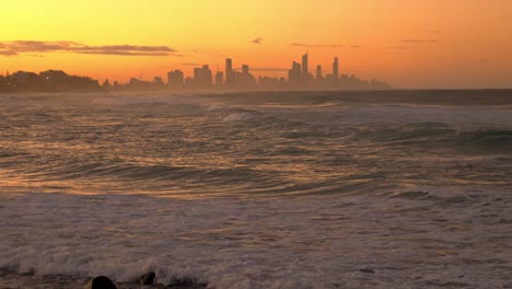 stunning landscape of golden sunset over the ocean - surfers surfing at the australian beach - surfers paradise in the background - gold coast, qld, australia.  - wide shot