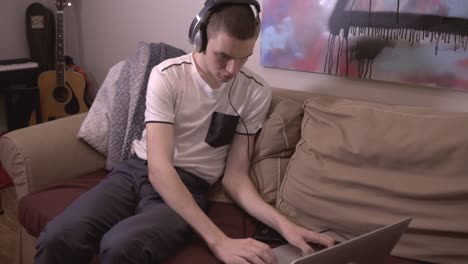 young man sitting on the sofa and working with his laptop while listening to music at home