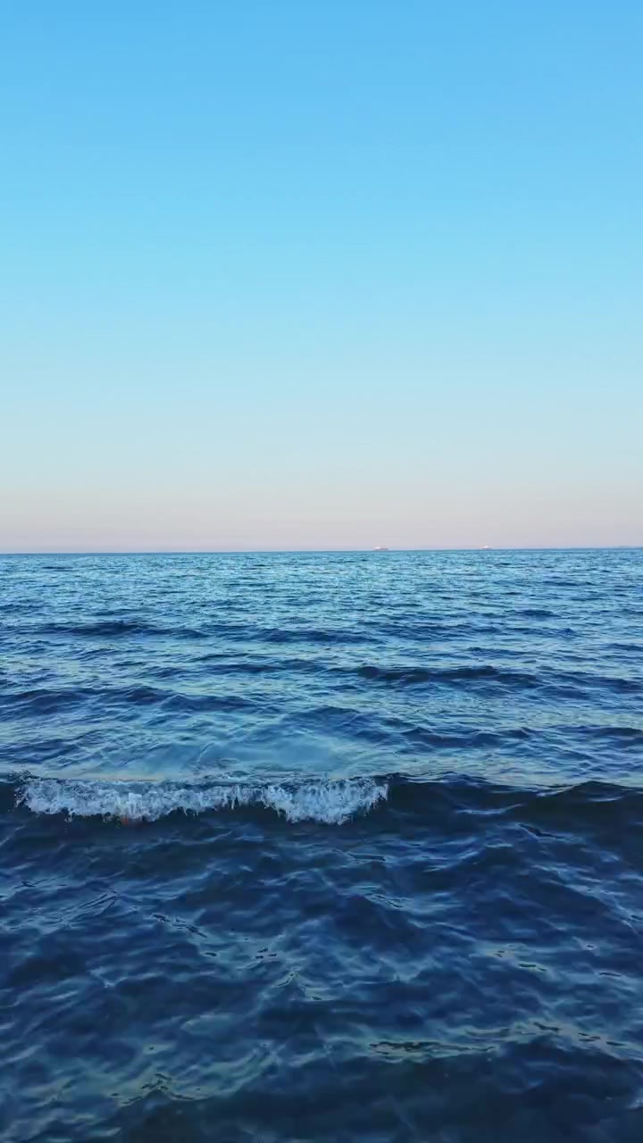 Wide view of the calm ocean waves under a clear sky during sunset near a beach