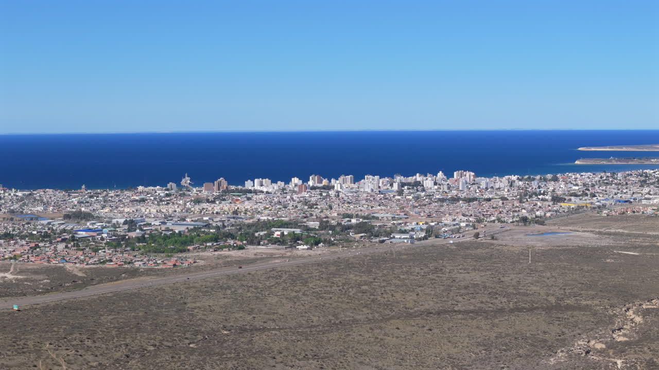 Aerial view of Puerto Madryn city in Patagonia, showcasing urban development, coastal landscape, and the vast expanse of the Atlantic Ocean under a clear blue sky, Biedma, Chubut, Argentina