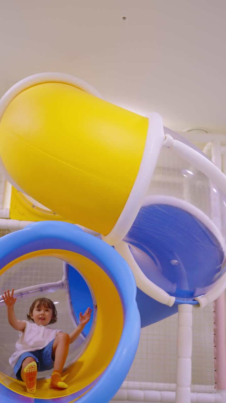 Child emerging from a vibrant yellow and blue tunnel slide at a modern indoor playground
