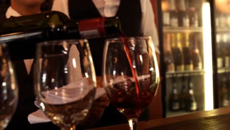 Mid-section-of-waitress-pouring-red-wine-on-a-glass