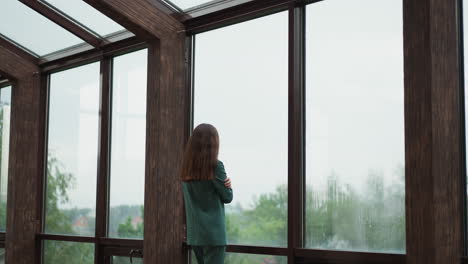 a woman in a green suit stands by a window looking out at the rain