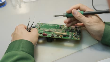 electronic equipment repair shop. the engineer technician solders the printed circuit board of an electronic device under a microscope.